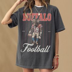 This retro Buffalo football t-shirt features a vintage illustration of a Buffalo holding a football dressed as a football player. This tee is the perfect gift for football fans or anybody who loves a good buffalo and football. This shirt is not associated with any team or league and is simply a piece of sports memorabilia for football fans in buffalo. This retro pinstripe football graphic t-shirt is an awesome piece of buffalo football merch for any sports fan or member of the mafia. This retro Retro Tops For Football Season Streetwear, Retro Tops For Streetwear During Football Season, Football Season Fan Apparel T-shirt With Screen Print, Football Season Fan Merchandise T-shirt, Vintage Graphic Print T-shirt For Sports Events, Football Season Fan Gear Graphic Top, Football Season Fan Merchandise Graphic Tee, Football Season Fan Apparel Tops With Graphic Print, Football Season Graphic Tee With Short Sleeves