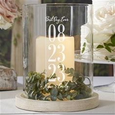 a candle that is sitting inside of a glass container on a table with flowers in the background