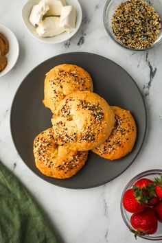 three bagels on a black plate with strawberries and cream cheese in bowls next to them