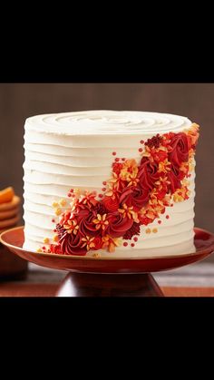 a white cake with red and yellow flowers on it sitting on a wooden table next to crackers