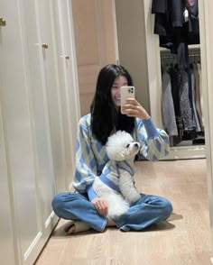 a woman sitting on the floor taking a selfie with her cell phone while holding a dog