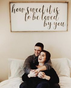 a man and woman sitting on top of a bed next to a sign that says how sweet it is to be loved by you