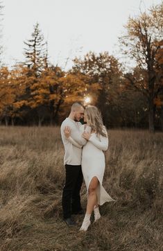 an engaged couple standing in the middle of a field with their arms around each other