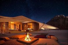 an outdoor fire pit in front of a house at night with mountains in the background