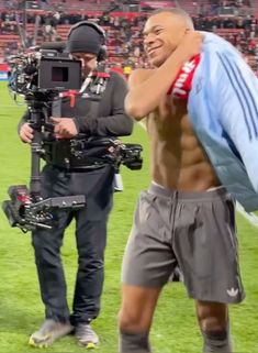 a shirtless man holding a camera on top of a field