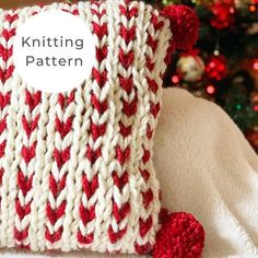 a red and white knitted pillow sitting next to a christmas tree