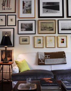 a living room filled with lots of framed pictures on the wall above a white couch