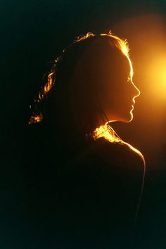 a woman is silhouetted against the sun with her hair blowing in the wind,