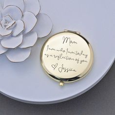 a white plate with a flower and a gold compact mirror on it that says mom