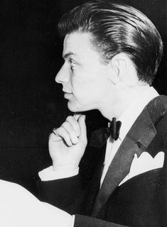 a man in a suit and bow tie sitting at a table with his hand on his chin