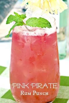 a pink drink in a glass sitting on top of a checkered table cloth next to a yellow flower