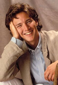 a young man is smiling while sitting down with his hand on his head and looking at the camera