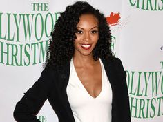 a woman with curly hair standing in front of a hollywood christmas tree sign and smiling at the camera