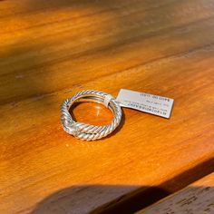 a silver ring sitting on top of a wooden table next to a metal tag that says,