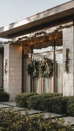 two wreaths are hanging on the front door of a house with lights and greenery