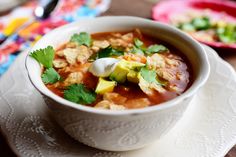 a bowl of soup with tortilla chips and sour cream in it on a plate