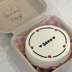 a white cake in a box with writing on the top and red hearts around it