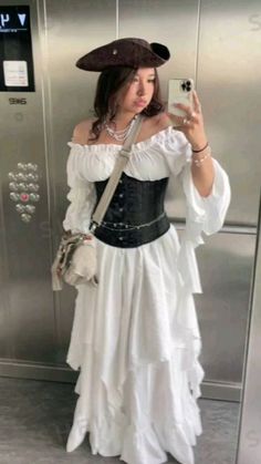 a woman in a white dress taking a selfie with her cell phone while wearing a pirate hat