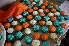 several cupcakes are arranged on a table with orange and blue frosted flowers