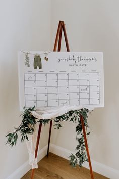 an easel with a calendar on it sitting in front of a white wall and wooden floor