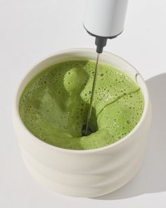 a green liquid in a white bowl being stirred with an electric blender