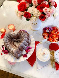 a heart shaped bunt cake sitting on top of a table next to bowls of strawberries