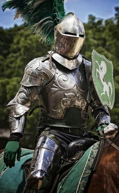 a man dressed in armor riding on the back of a horse wearing a green feathered hat