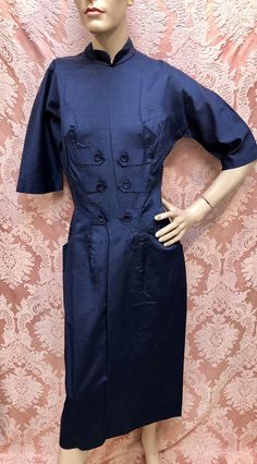 Vintage 1950s Classic "Hot Secretary" Navy Blue Hour-Glass Wiggle Dress with Decorative Tab Front accented with Donut Buttons & Two Slash Front Hip Pockets. 3/4-Length Raglan sleeves, Full Rear Metal Zipper, Partial Cotton liner in the skirt. The Fabric feels like a smooth silky blend of cotton and rayon, almost like a polished cotton but I believe there's a hint of rayon in the weave, there is a slub in the weave similar to shantung. Dress is likely Deadstock, from the estate of the ultimate pa Blue 1950s Style Knee-length Vintage Dress, Blue Knee-length Vintage Dress 1950s Style, Blue Knee-length 1950s Vintage Dress, Navy Fitted Vintage Dress, 1950s Style Fitted Dress With Buttons, Navy Vintage Dress With Buttons, Navy Vintage Short Sleeve Dress, Navy Vintage Dresses With Buttons, 1950s Fitted Vintage Dress For Work