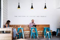 two people sitting at a table with laptops in front of them and the wall behind them reads the pattern of coffee and people