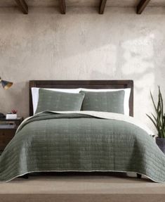 a bed with green bedspread and pillows next to a potted plant on a table