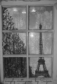 the eiffel tower seen through a window in black and white with snow falling on it