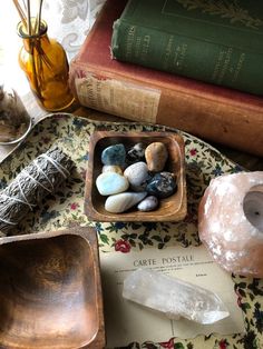 some rocks are in a bowl on a table next to books and other items that include candles