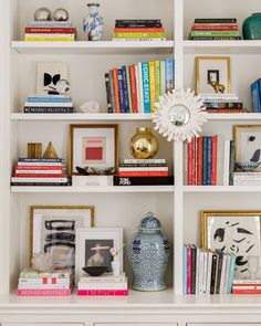 a white book shelf filled with books and vases on top of eachother