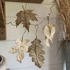 three dried leaves hanging from a wire on a wall next to a potted plant