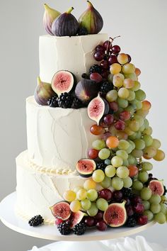 a wedding cake with figurines, grapes and figs on the top tier