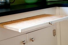 a wooden cutting board sitting on top of a white cabinet in a kitchen with black counter tops