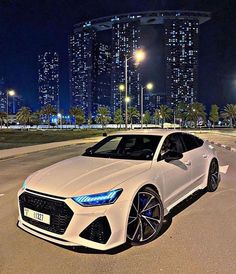 a white car is parked in an empty parking lot at night with city lights behind it