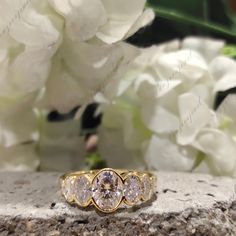 three stone ring sitting on top of a rock with white flowers in the back ground