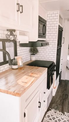 a white kitchen with black appliances and wood counter tops in the center, along with an area rug on the floor