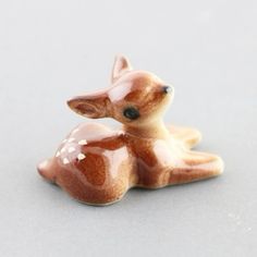 a small ceramic deer figurine sitting on the ground with its eyes closed and nose open