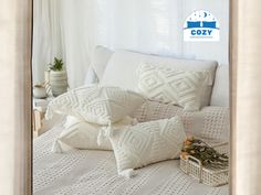 pillows on a bed with white linens in the background and a blue sign that says cozy