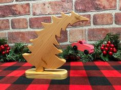 a wooden christmas tree with a toy car in front of it on a red and black checkered tablecloth