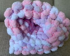 a pink and white object sitting on top of a couch next to a pillow covered in pom - poms