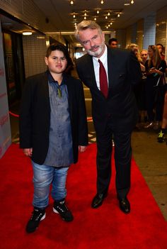 a man in a suit and tie standing next to a boy on a red carpet