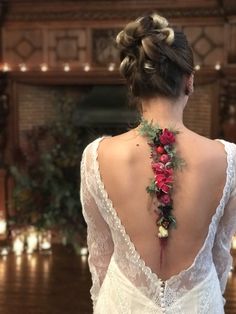 the back of a woman's wedding dress with flowers on it and candles in the background