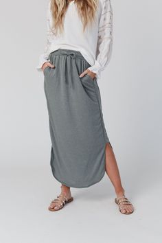 a woman in a white top and grey skirt is standing with her hands on her hips