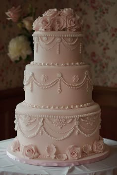 a three tiered wedding cake with pink flowers on the top and pearls on the bottom