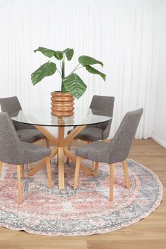 a glass table with four chairs and a potted plant on top in front of a curtained window