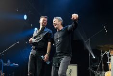 two men are standing on stage with their arms in the air and one man is raising his fist