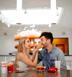 a man and woman sitting at a table with food in front of them, eating pizza